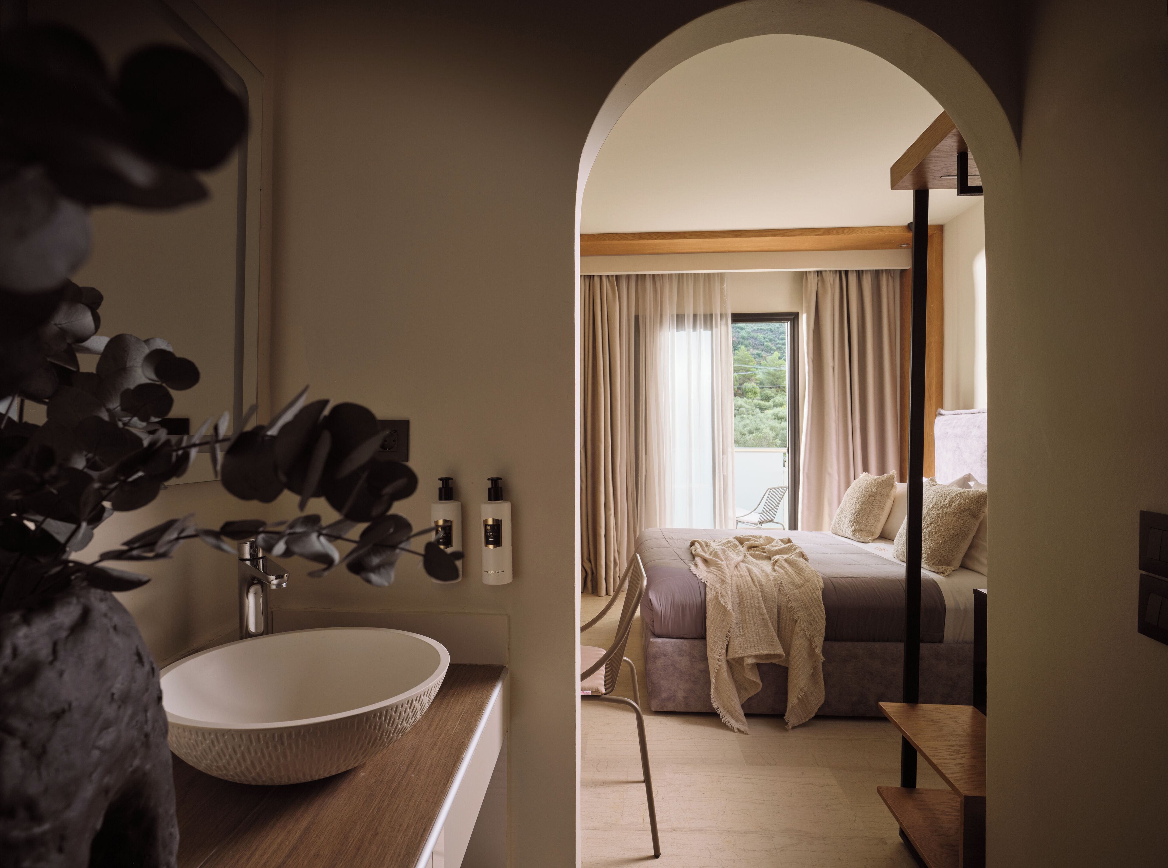 Ein modernes Badezimmer mit einem großen Waschbecken, einem Spiegel und einer Pflanze. Es geht zu einem Schlafzimmer mit einem Bett, einem Fenster und einem Balkon.