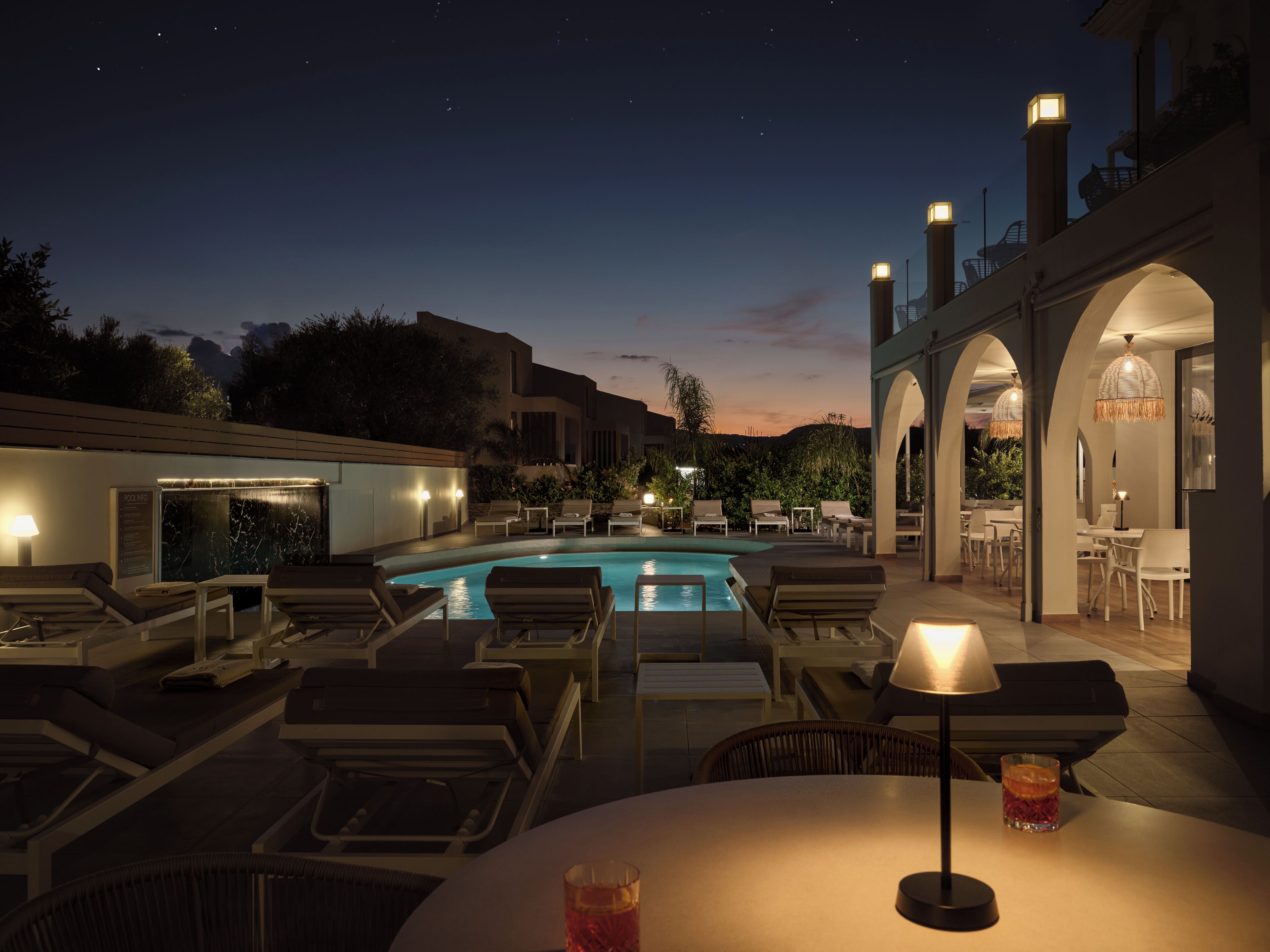 A poolside area with lounge chairs, a pool, and a dining area with tables and chairs.