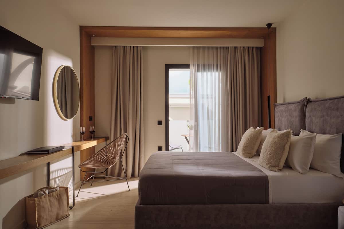 A hotel room with a bed, a desk with a chair, a TV, and a window with curtains.