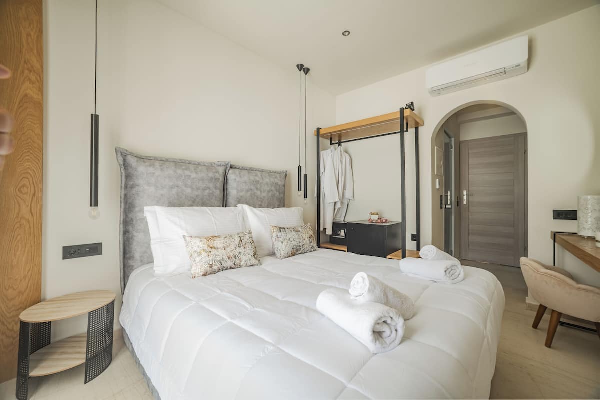 A modern bedroom with a large bed, a wooden side table, a mirror, and a wardrobe.