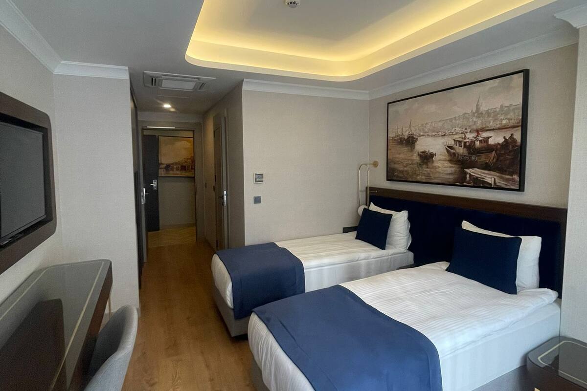 A hotel room with two beds, a desk, and a TV.