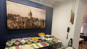 A buffet setup with various food items, a painting of a cityscape on the wall, and a phone on the wall. - Nevi Hotel & Suites İstanbul Taksim (Istanbul)