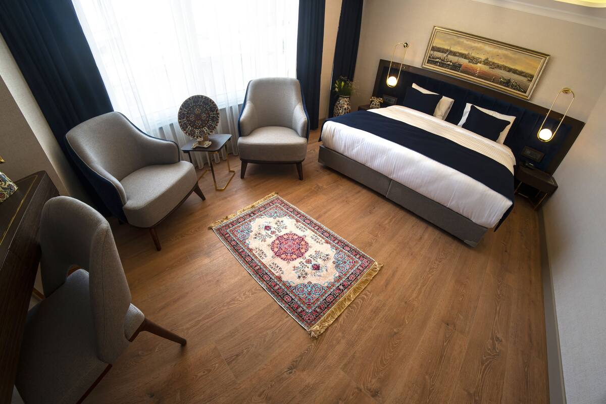 A hotel room with a large bed, two armchairs, a small table, and a decorative rug.