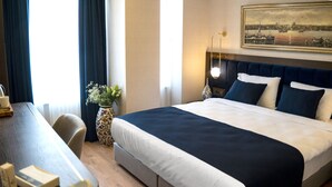 A hotel room with a large bed, a desk with a chair, a vase with flowers, and a painting on the wall. - Nevi Hotel & Suites İstanbul Taksim (Istanbul)