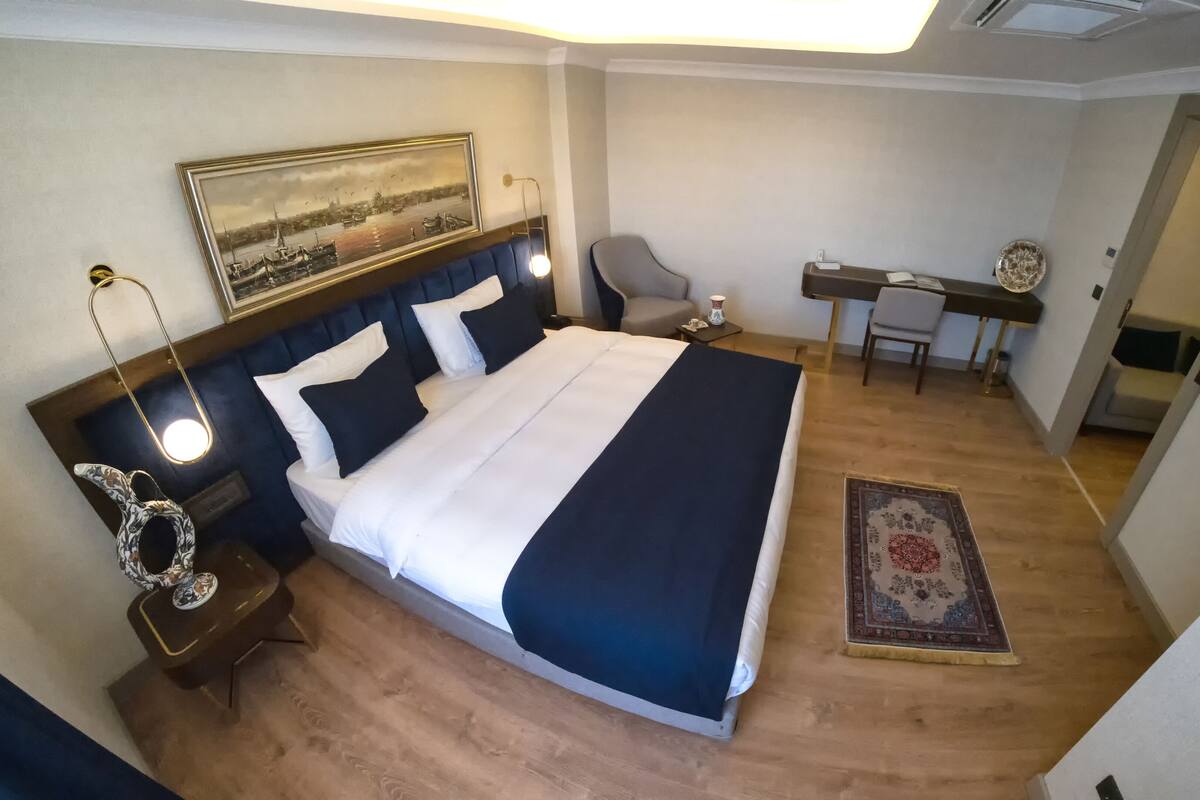 A hotel room with a large bed, a desk, a chair, a small table, and a painting on the wall.