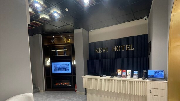 A hotel reception area with a reception desk, two armchairs, a small round table, and a television screen. - Nevi Hotel & Suites İstanbul Taksim (Istanbul)