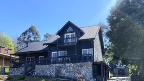 Un edificio de dos pisos con base de piedra, balcón y techo de metal.