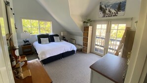 Un dormitorio con cama, escritorio, silla, ventilador de techo y ventana con vista a árboles.