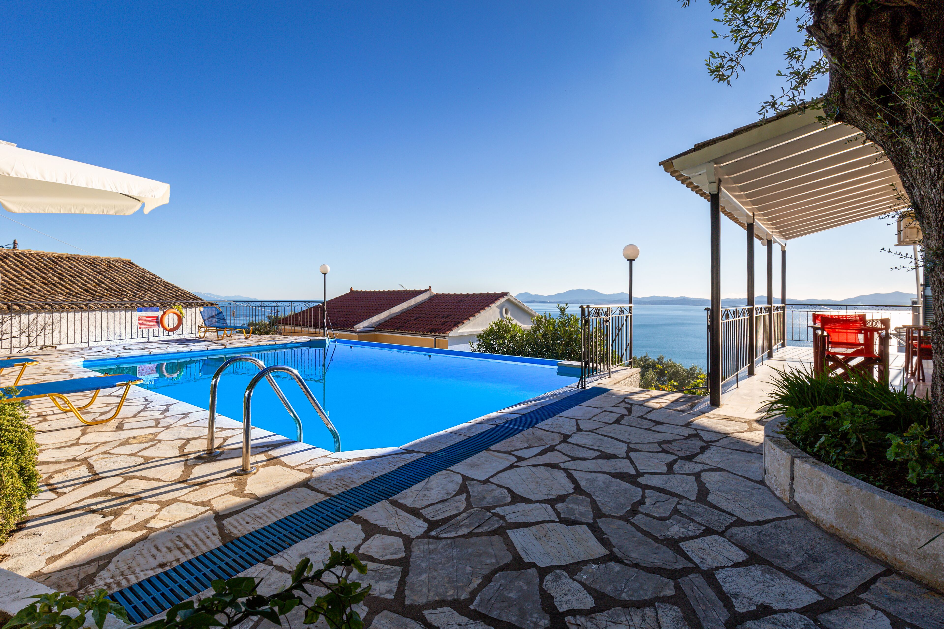 Una piscina con piastrelle in pietra, una zona relax coperta e vista sul mare.