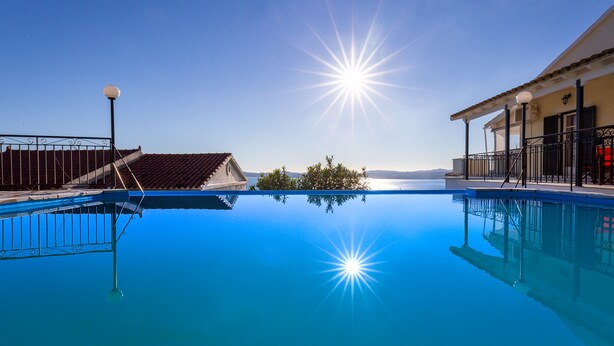 Ein klares, blaues Schwimmbecken mit Sonnenschein, ein Balkon und Meerblick.