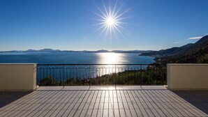 Eine Holzterrasse mit Metallgeländer, die auf ein Gewässer und ferne Berge blickt.