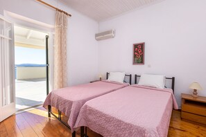 A bedroom with two beds, a window with a view, an air conditioner, and a nightstand with a lamp.