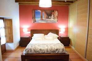 Un dormitorio con una cama de madera, dos mesitas de noche, una mesita auxiliar y una pared roja, con un cuadro enmarcado sobre la cama.