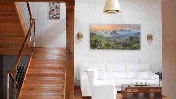 Un salon moderne avec un parquet en bois, un canapé blanc et un tableau représentant un paysage.