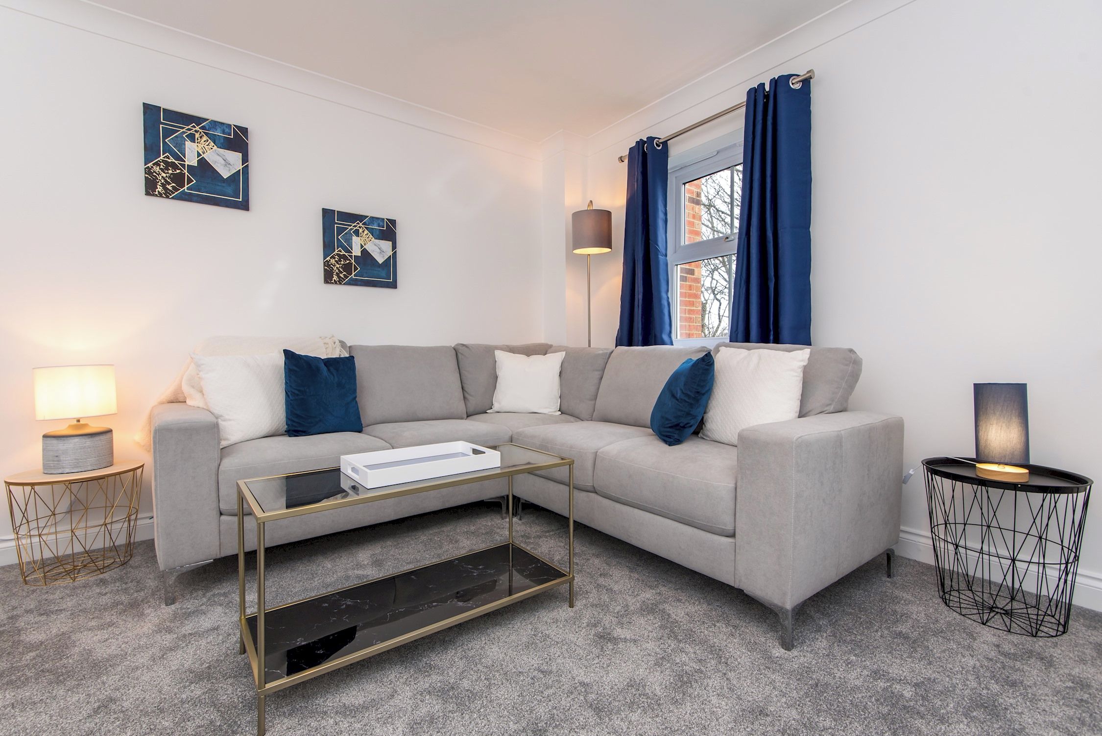 A modern living room with a grey sofa, a glass coffee table, and a side table with a lamp.