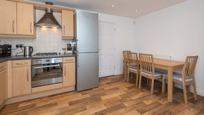 Une cuisine compacte dotée de meubles en bois, d’un réfrigérateur en acier inoxydable et d’un coin repas avec une table et des chaises en bois.
