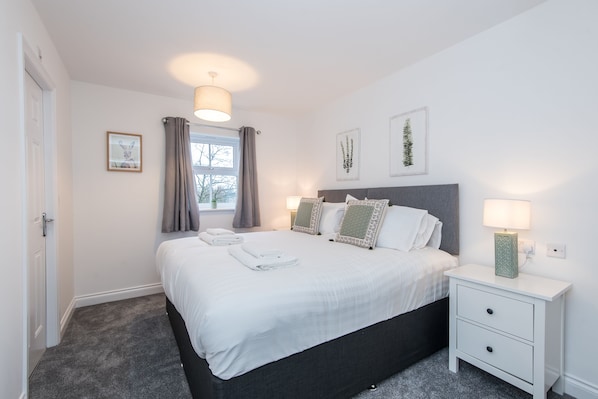 A bedroom with a bed, bedside tables, a window with curtains, and wall art.