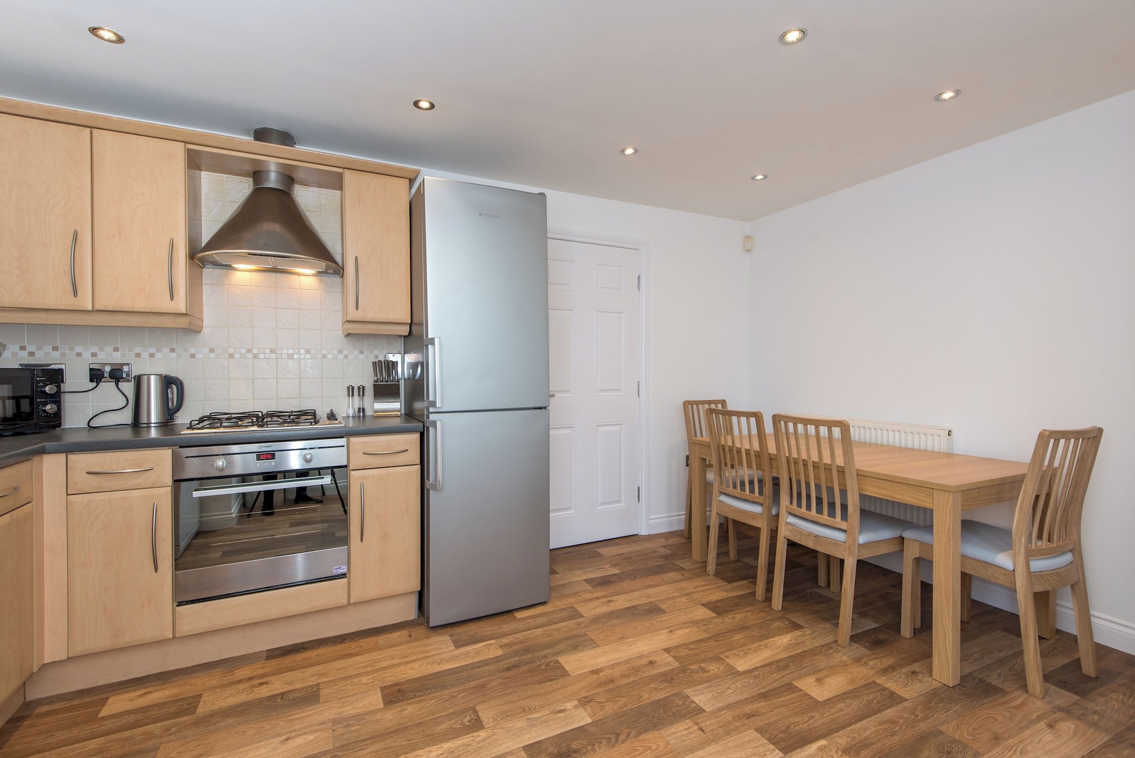 A compact kitchen with wooden cabinets, a stainless steel refrigerator, a gas stove, and a dining table with chairs.