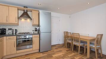A compact kitchen with wooden cabinets, a stainless steel refrigerator, a gas stove, and a dining table with chairs.