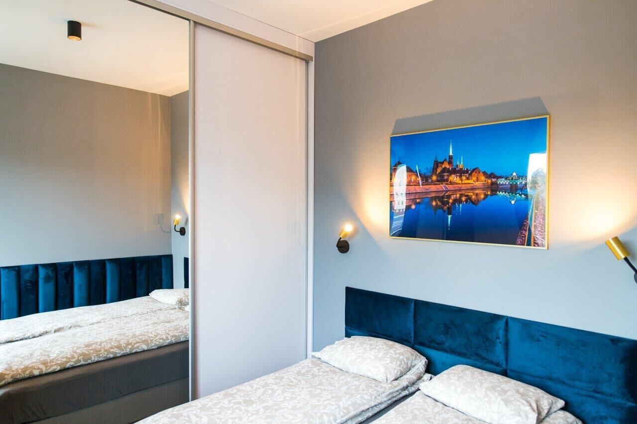 Habitación de hotel con dos camas, un espejo grande, un cuadro colgado en la pared con una vista urbana y lámparas de noche.