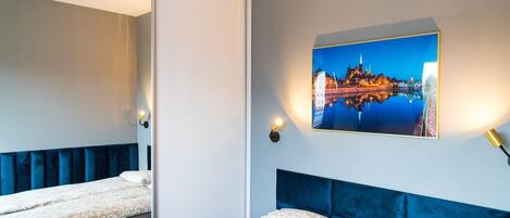 Habitación de hotel con dos camas, un espejo grande, un cuadro colgado en la pared con una vista urbana y lámparas de noche.