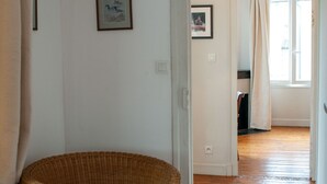 Une pièce avec un fauteuil en osier, un plancher en bois et une porte donnant sur une autre pièce.