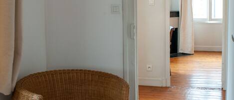 A room with a wicker chair, wooden flooring, and a doorway leading to another room.
