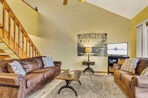 Un salon avec un canapé en cuir marron, une table basse, un téléviseur et une enseigne publicitaire pour un magasin de vente d’appâts situé près du lac Table Rock.