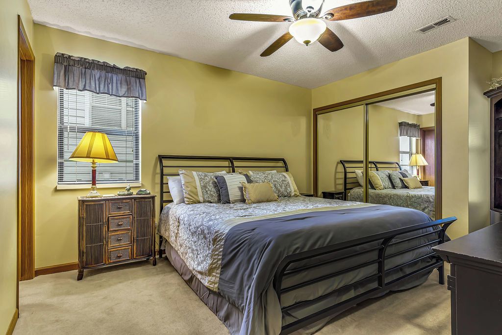 A bedroom with a bed, a nightstand, a dresser, a ceiling fan, and a large mirror.