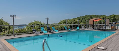 Une piscine rectangulaire avec une terrasse en bois, entourée de chaises longues et d’une clôture.
