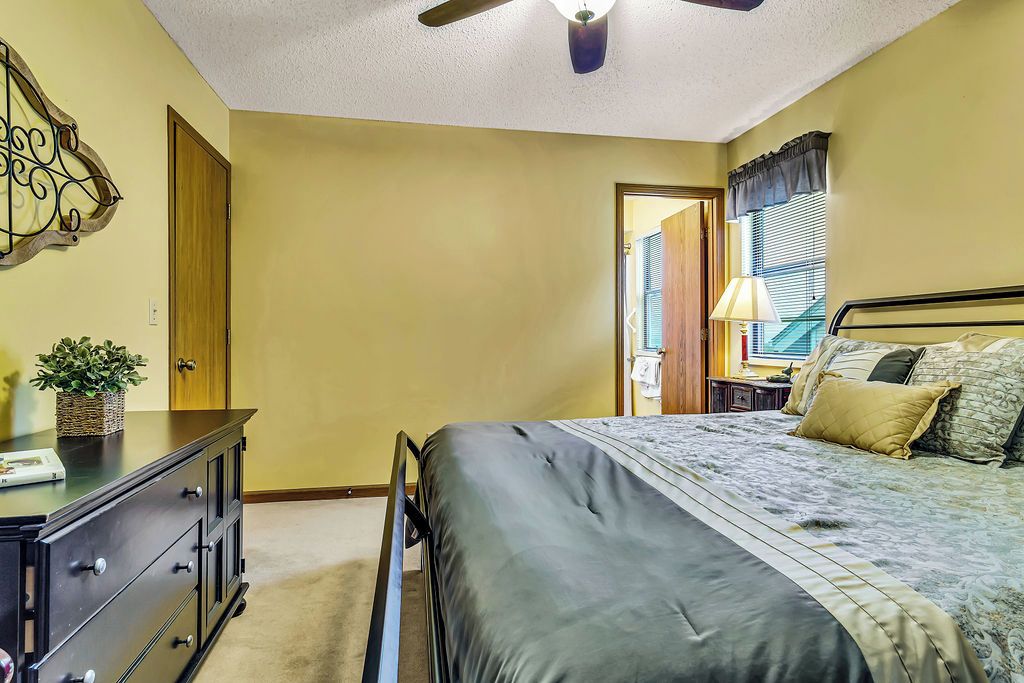 Une chambre à coucher comprenant un lit, une commode, un ventilateur de plafond et une fenêtre avec des stores.