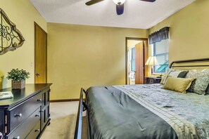 Une chambre à coucher comprenant un lit, une commode, un ventilateur de plafond et une fenêtre avec des stores.