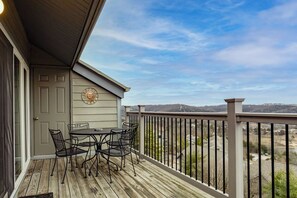 Un terrazzo in legno con tavolo e sedie, una porta con un elemento decorativo a parete, e vista su un paesaggio collinare.