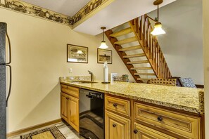Eine Küche mit Granit-Arbeitsplatten, Holzschränken, einem Geschirrspüler und einer Treppe, die in eine obere Etage führt.