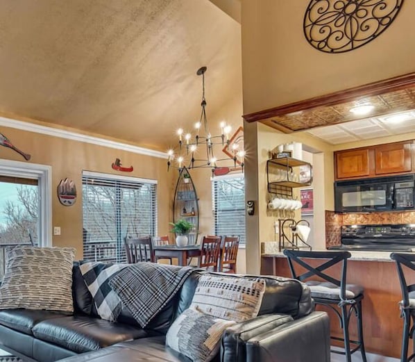 Relax in this inviting space with a comfortable sofa and dining area, featuring a modern kitchen with a stove and cabinets.