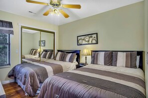 A hotel room with two beds, a ceiling fan, a large mirror, and artwork on the wall.