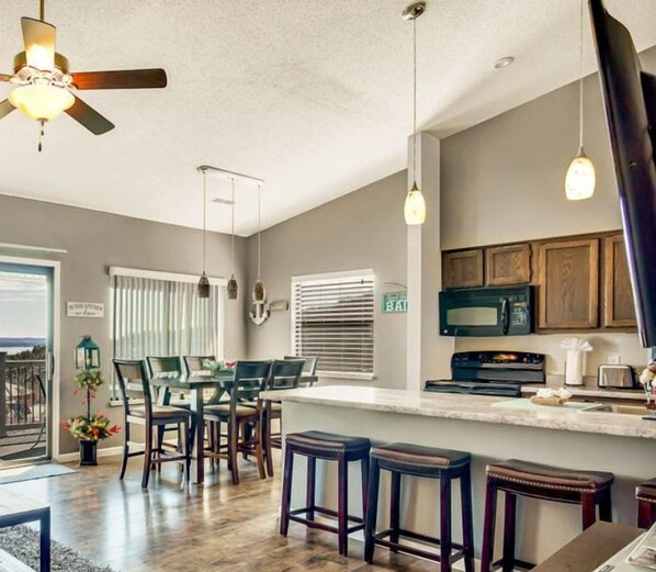 A modern kitchen with a central island, bar stools, and a ceiling fan.