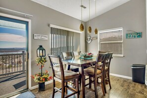 A dining area with a table and chairs, a view through a door, and a sign on the wall.