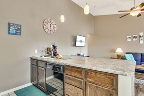 A kitchen with a central island, wooden cabinets, a dishwasher, and a clock on the wall.
