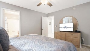 Ein Schlafzimmer mit Bett, Kommode, Deckenventilator und Fernseher mit einem Logo.