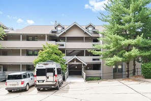 A multi-story building with a central entrance, parking area, and a tree to the right. - Lake View Condo, Spacious & Only 1 Mile to Silver Dollar City – 1204 (Branson)