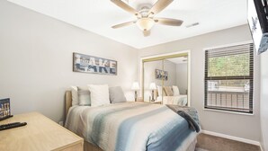 A bedroom with a bed, a ceiling fan, a bedside table, a lamp, a mirror, and a window with blinds. - Lake View Condo, Spacious & Only 1 Mile to Silver Dollar City – 1204 (Branson)