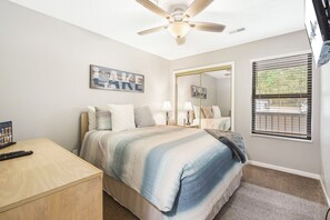 A bedroom with a bed, bedside tables, a ceiling fan, a window with blinds, and a door with a mirror. - Lake View Condo, Spacious & Only 1 Mile to Silver Dollar City – 1204 (Branson)