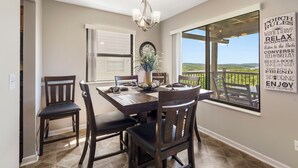 A dining area with a table and chairs, a chandelier, a window with a view, and a wall with motivational text. - Lake View Condo, Spacious & Only 1 Mile to Silver Dollar City – 1204 (Branson)