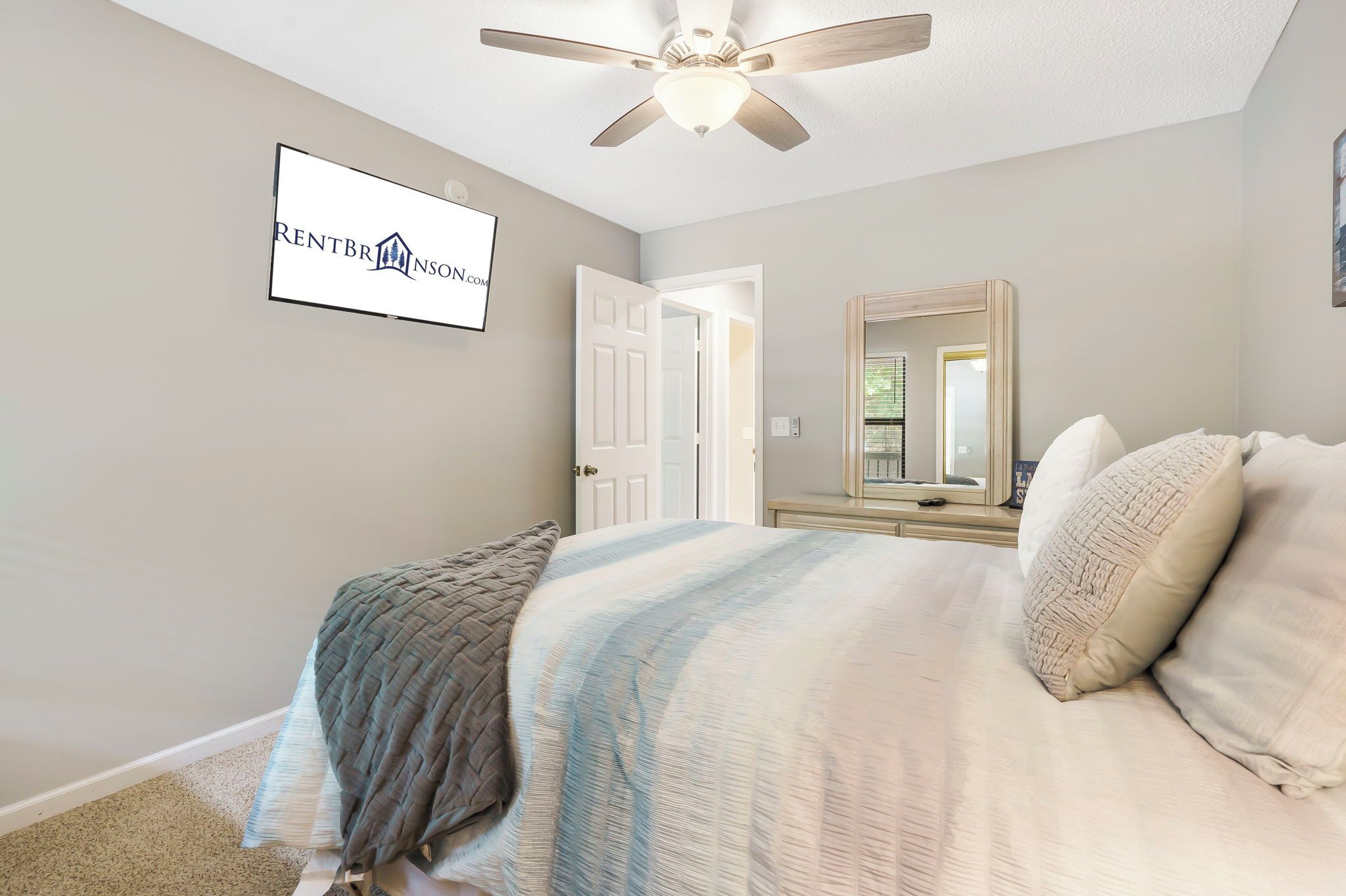 A bedroom with a bed, a ceiling fan, a door, and a mirror.