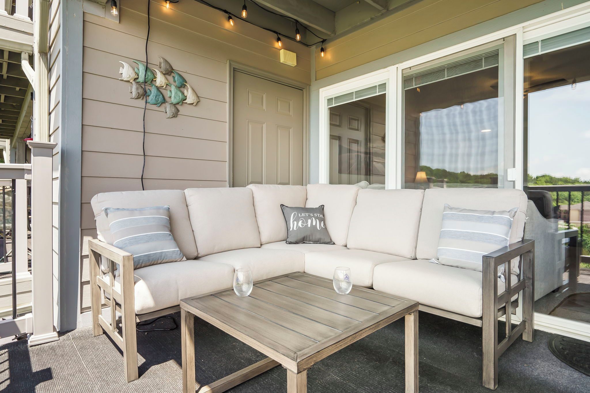 A sectional sofa with a glass coffee table, a decorative wall with lights, and a view through a glass door.