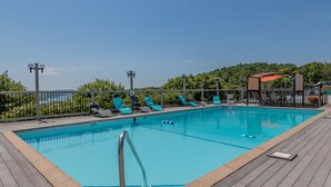 Ein rechteckiger Pool mit Holzterrasse, umgeben von Liegestühlen und einem Metallzaun.