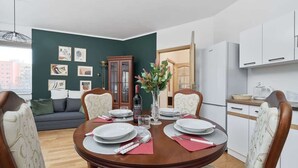 Un área de comedor con una mesa redonda preparada para cuatro personas, rodeada de sillas tapizadas. Se ve un aparador de madera y una puerta con panel de vidrio al fondo.