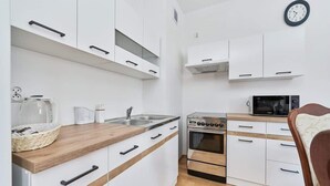 Cocina compacta con armarios blancos, encimera de madera, microondas, horno y un reloj en la pared.