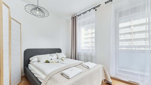 Un dormitorio moderno con cama, lámpara colgante, cortinas translúcidas y vistas al exterior.